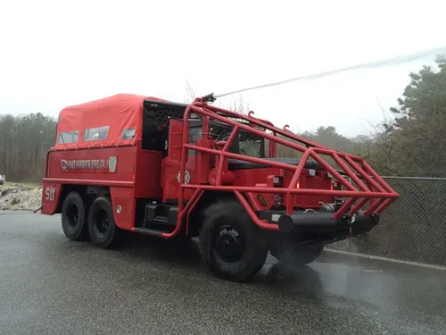 Exterior view of small fire truck showing cab, body compartments, and wheel/tire area.