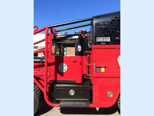 Exterior view of small fire truck showing cab, body compartments, and wheel/tire area.
