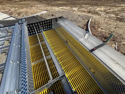 Top walkway view toward rear with yellow grating and side rails.