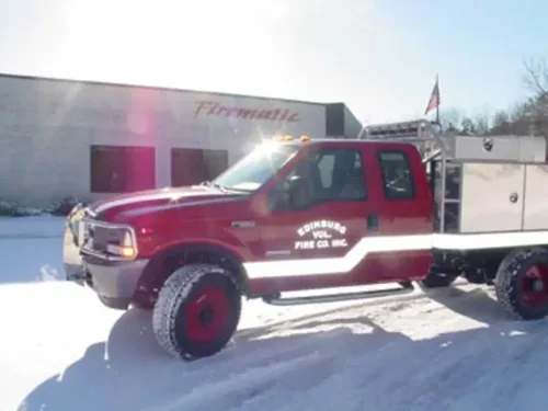 Exterior view of small fire truck showing cab, body compartments, and wheel/tire area.