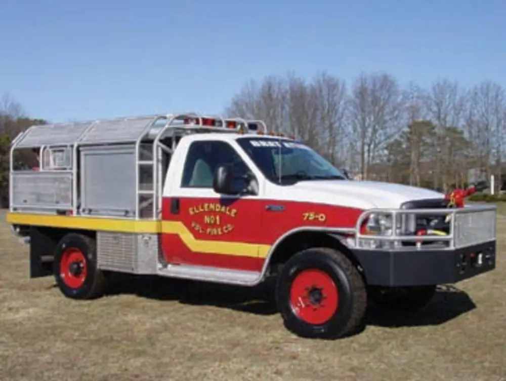 Exterior view of small fire truck showing cab, body compartments, and wheel/tire area.