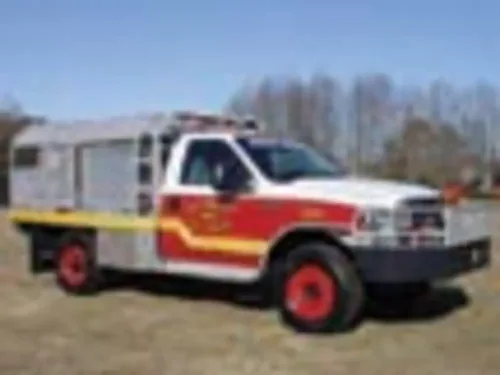Exterior view of small fire truck showing cab, body compartments, and wheel/tire area.