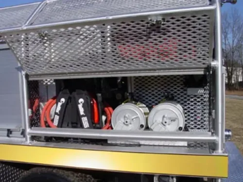 Exterior view of small fire truck showing cab, body compartments, and wheel/tire area.