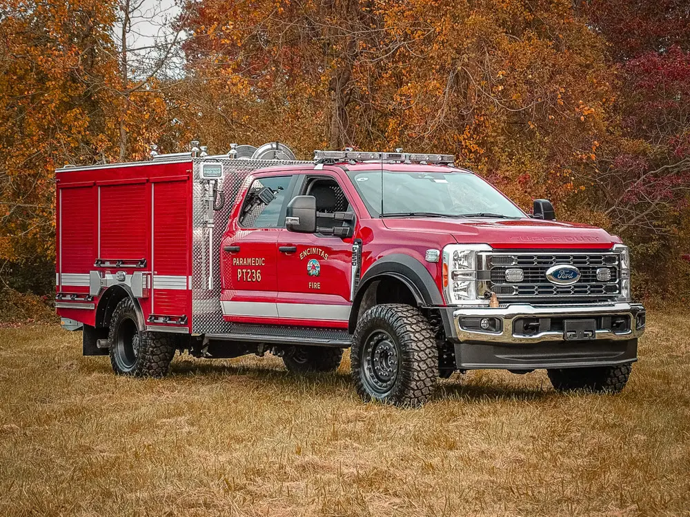 Front three-quarter view of red brush fire truck on grass.