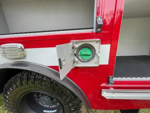 Close-up of side utility outlet with green cap and open hatch.