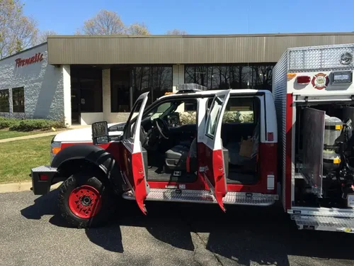 Exterior view of small fire truck showing cab, body compartments, and wheel/tire area.