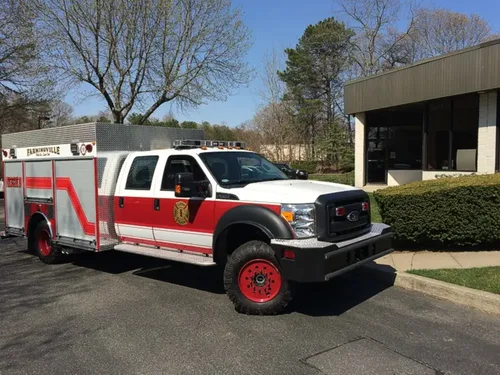 Exterior view of small fire truck showing cab, body compartments, and wheel/tire area.
