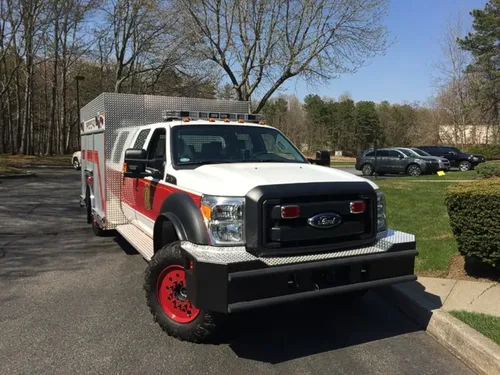 Exterior view of small fire truck showing cab, body compartments, and wheel/tire area.