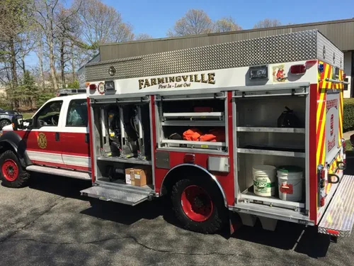 Exterior view of small fire truck showing cab, body compartments, and wheel/tire area.