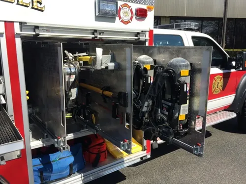 Exterior view of small fire truck showing cab, body compartments, and wheel/tire area.