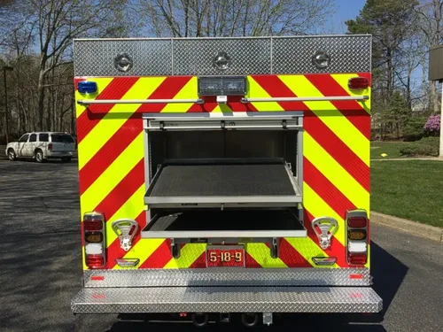 Exterior view of small fire truck showing cab, body compartments, and wheel/tire area.