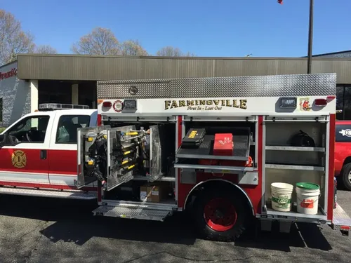 Exterior view of small fire truck showing cab, body compartments, and wheel/tire area.