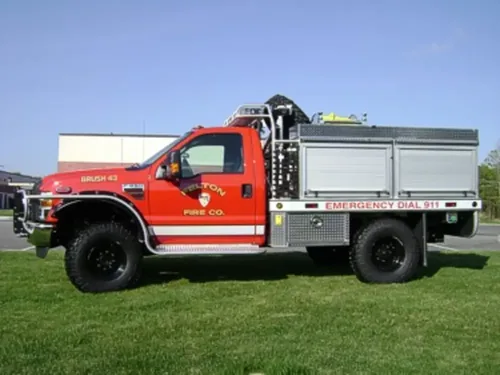 Exterior view of small fire truck showing cab, body compartments, and wheel/tire area.