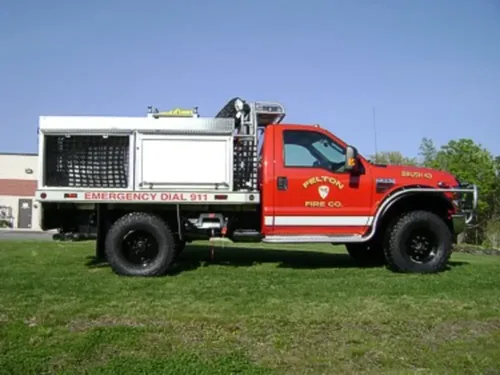 Exterior view of small fire truck showing cab, body compartments, and wheel/tire area.