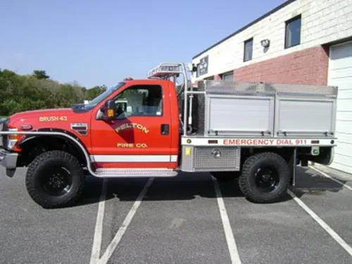 Exterior view of small fire truck showing cab, body compartments, and wheel/tire area.