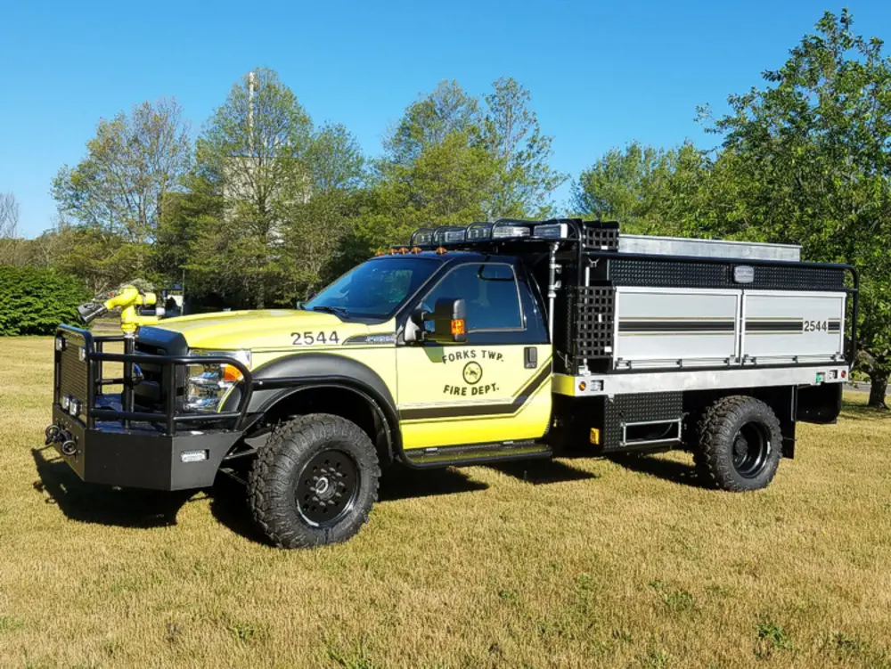 Exterior view of small fire truck showing cab, body compartments, and wheel/tire area.