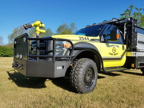 Exterior view of small fire truck showing cab, body compartments, and wheel/tire area.