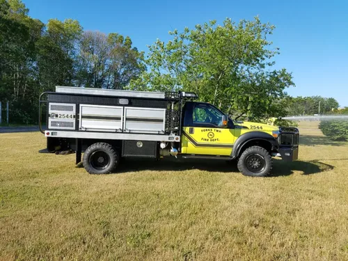 Exterior view of small fire truck showing cab, body compartments, and wheel/tire area.