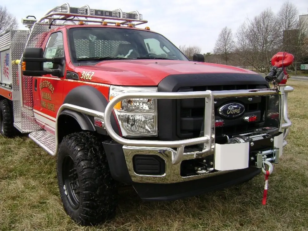 Exterior view of small fire truck showing cab, body compartments, and wheel/tire area.