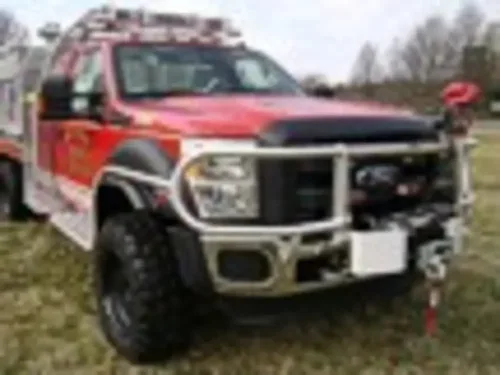 Exterior view of small fire truck showing cab, body compartments, and wheel/tire area.