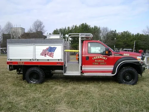 Exterior view of small fire truck showing cab, body compartments, and wheel/tire area.