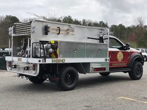 Exterior view of small fire truck showing cab, body compartments, and wheel/tire area.