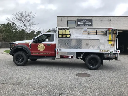 Exterior view of small fire truck showing cab, body compartments, and wheel/tire area.