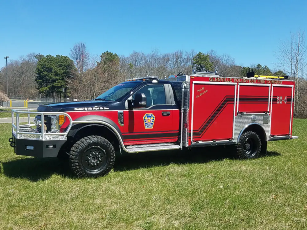 Exterior view of small fire truck showing cab, body compartments, and wheel/tire area.