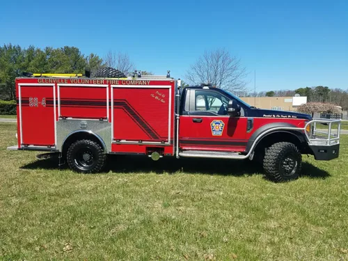 Exterior view of small fire truck showing cab, body compartments, and wheel/tire area.