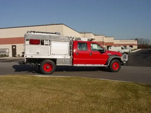Exterior view of small fire truck showing cab, body compartments, and wheel/tire area.