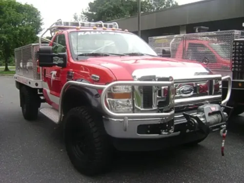 Exterior view of small fire truck showing cab, body compartments, and wheel/tire area.