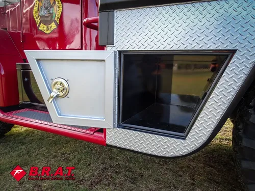 Exterior view of small fire truck showing cab, body compartments, and wheel/tire area.