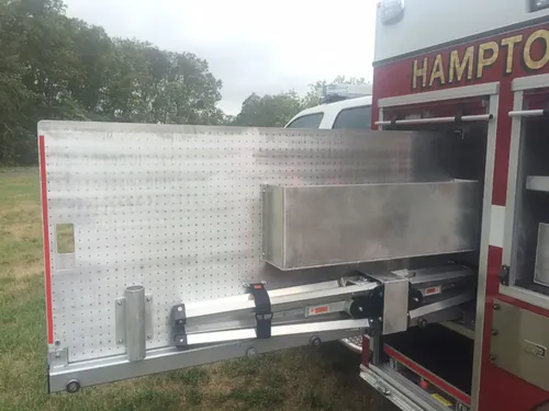 Exterior view of small fire truck showing cab, body compartments, and wheel/tire area.