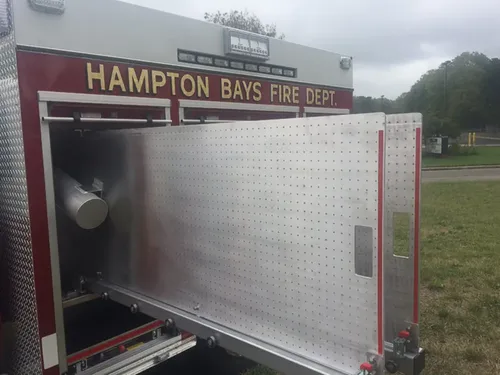 Exterior view of small fire truck showing cab, body compartments, and wheel/tire area.