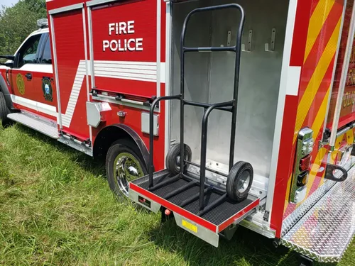 Exterior view of small fire truck showing cab, body compartments, and wheel/tire area.