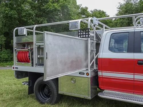 Exterior view of small fire truck showing cab, body compartments, and wheel/tire area.