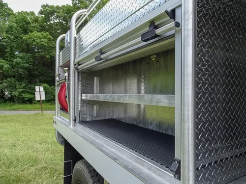 Exterior view of small fire truck showing cab, body compartments, and wheel/tire area.