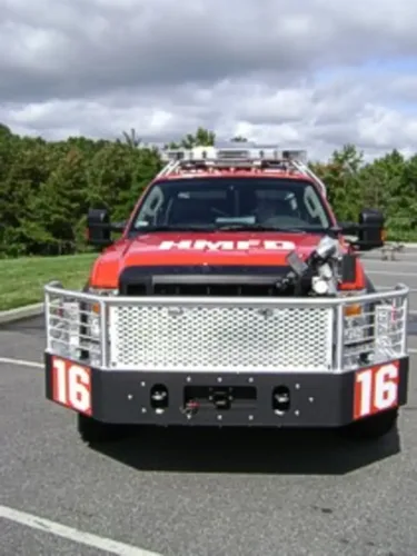 Exterior view of small fire truck showing cab, body compartments, and wheel/tire area.