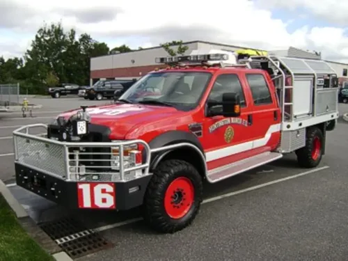 Exterior view of small fire truck showing cab, body compartments, and wheel/tire area.