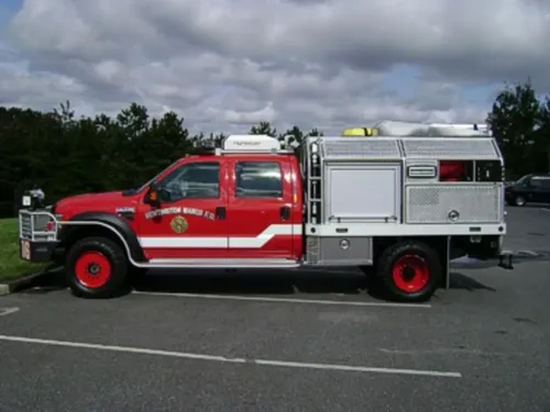 Exterior view of small fire truck showing cab, body compartments, and wheel/tire area.