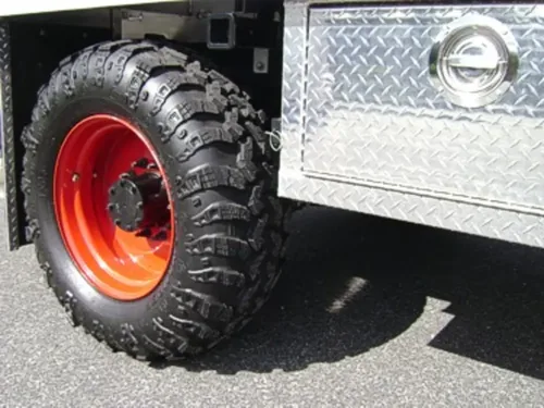Exterior view of small fire truck showing cab, body compartments, and wheel/tire area.