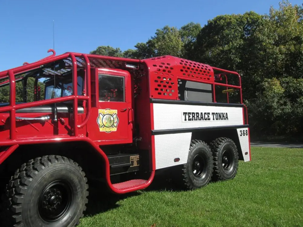 Exterior view of small fire truck showing cab, body compartments, and wheel/tire area.