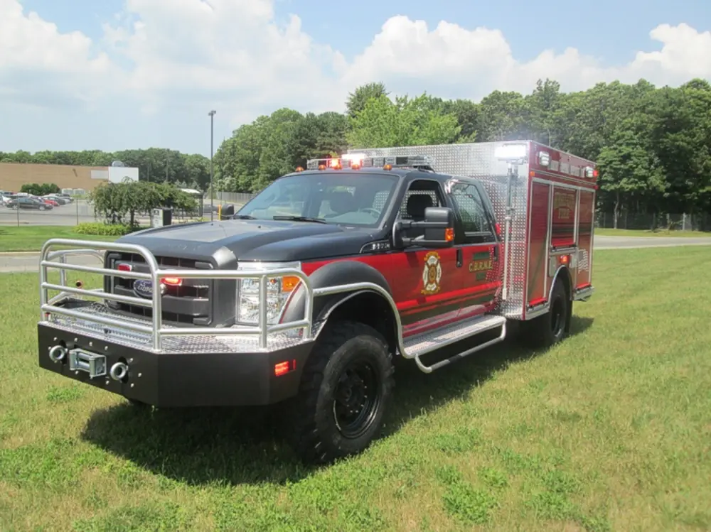 Exterior view of small fire truck showing cab, body compartments, and wheel/tire area.