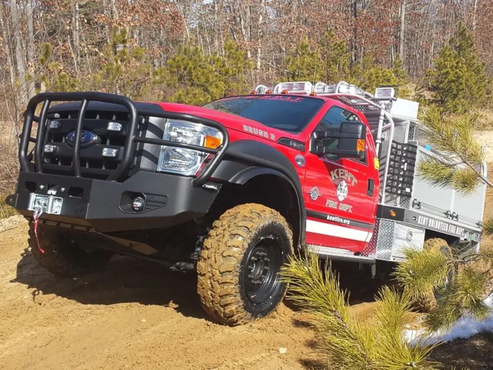 Exterior view of small fire truck showing cab, body compartments, and wheel/tire area.