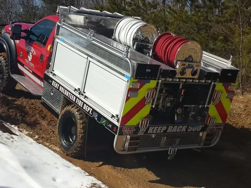 Exterior view of small fire truck showing cab, body compartments, and wheel/tire area.