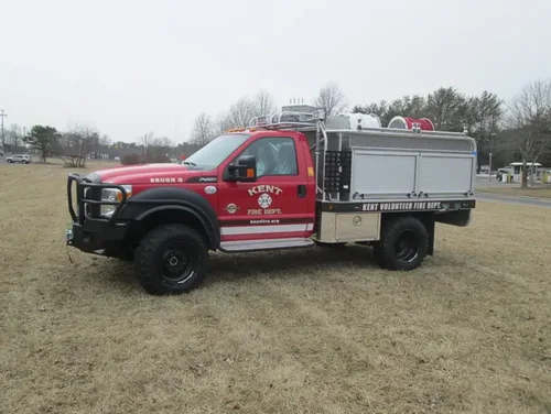 Exterior view of small fire truck showing cab, body compartments, and wheel/tire area.