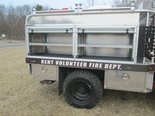 Exterior view of small fire truck showing cab, body compartments, and wheel/tire area.