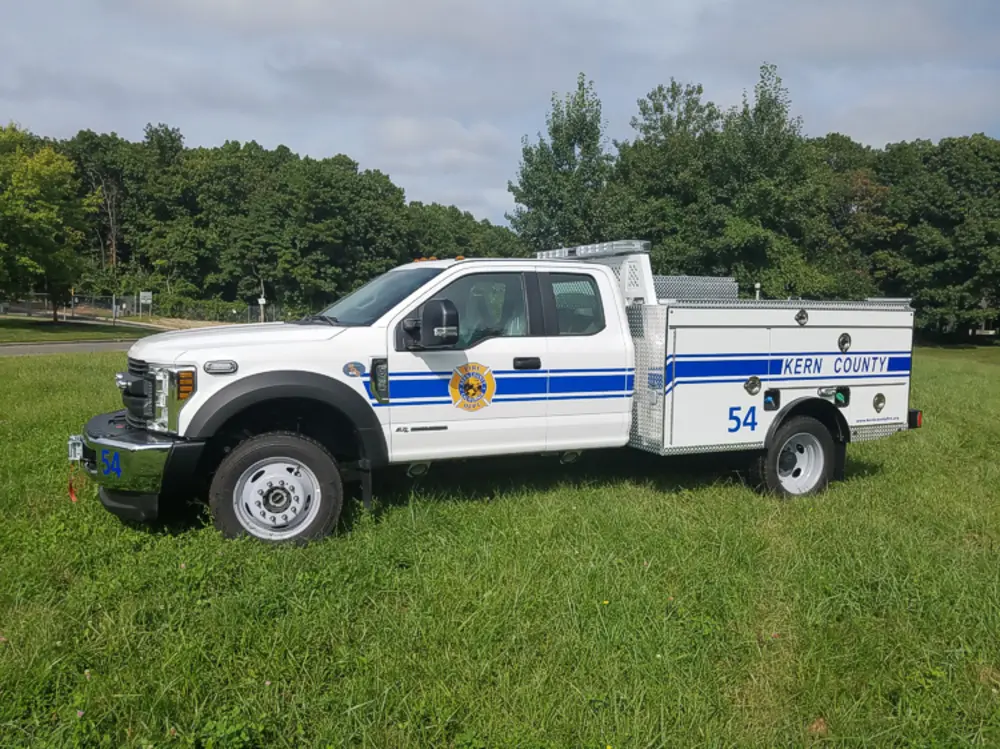 Exterior view of small fire truck showing cab, body compartments, and wheel/tire area.