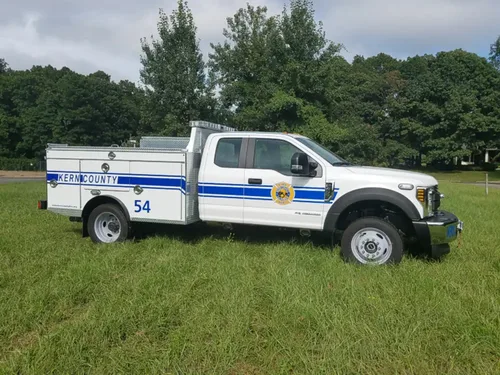 Exterior view of small fire truck showing cab, body compartments, and wheel/tire area.