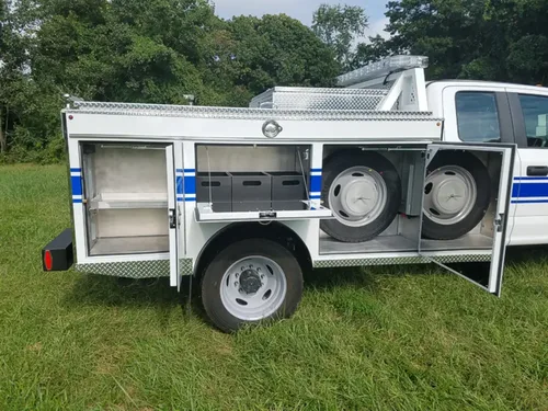 Exterior view of small fire truck showing cab, body compartments, and wheel/tire area.